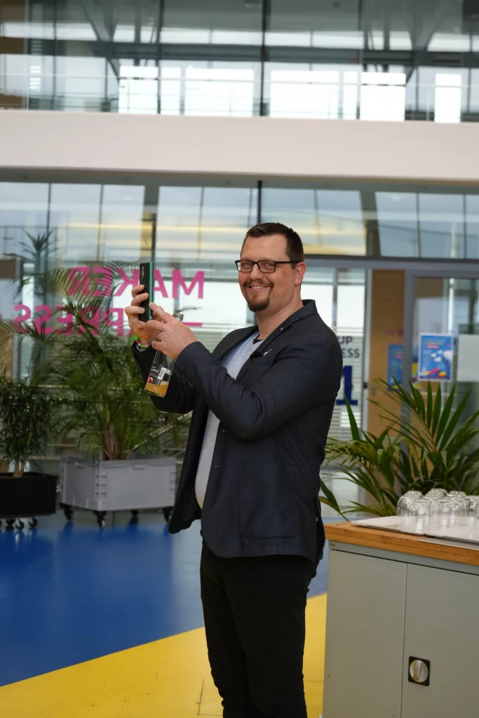 Martin Jäger, Gründer und Organisator des KI Roundtable #3 in Böblingen, lächelt in die Kamera und hält eine Flasche.